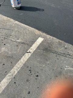 Parking lot pavement with a white line, curb, and a blurred hand at the bottom right