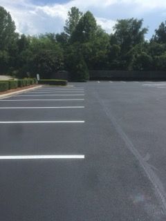 Empty parking lot with white parking lines and trees along the far edge under a partly cloudy sky