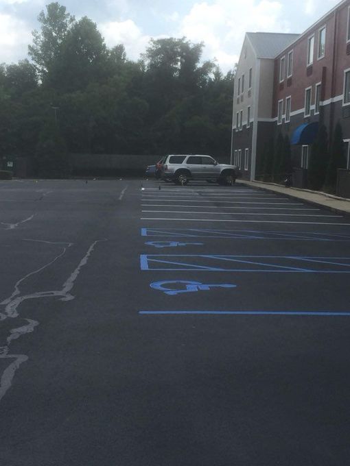 Empty parking lot with blue accessible parking markings beside a building and parked SUV