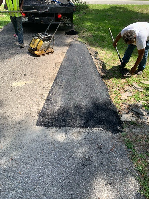 Workers patching a cracked driveway with fresh asphalt next to a parked truck
