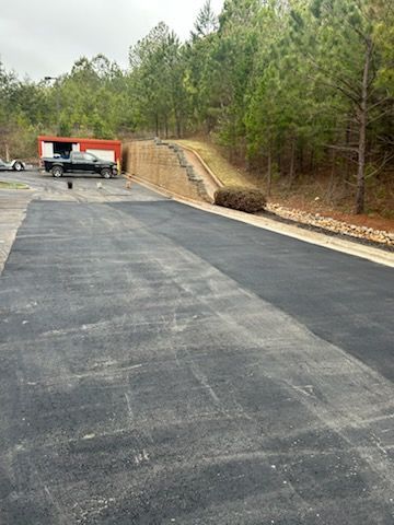 Empty parking lot beside a wooded hillside with a utility truck and retaining wall