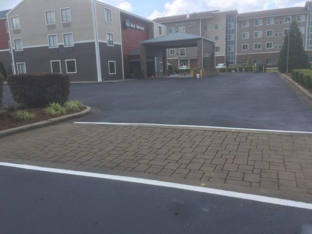 Apartment complex driveway and entrance with brick paving and parked area in front of buildings