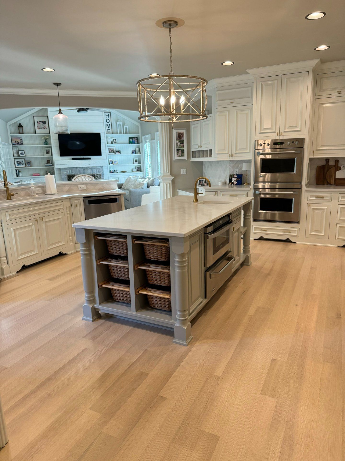 Bright kitchen with white cabinetry, light wood floors, and a large island with built-in microwave and storage baskets.