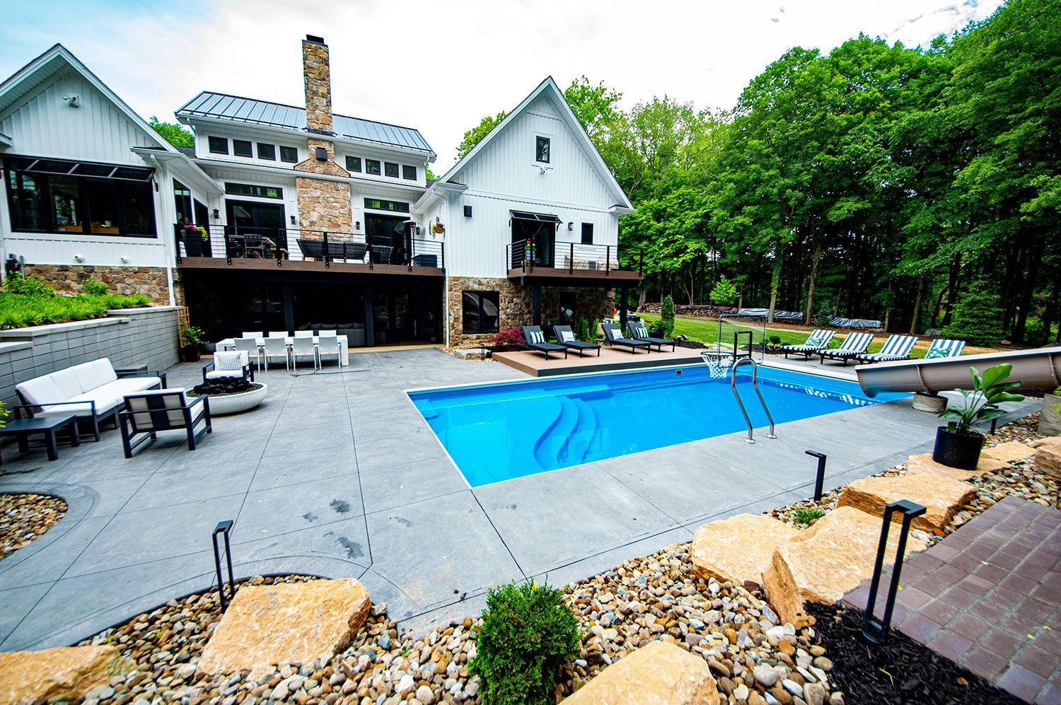 White modern home with a swimming pool and patio in a wooded area.