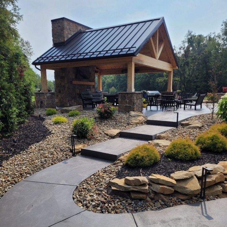 Outdoor patio with stone fireplace, wooden beams, black metal roof, and stone steps.