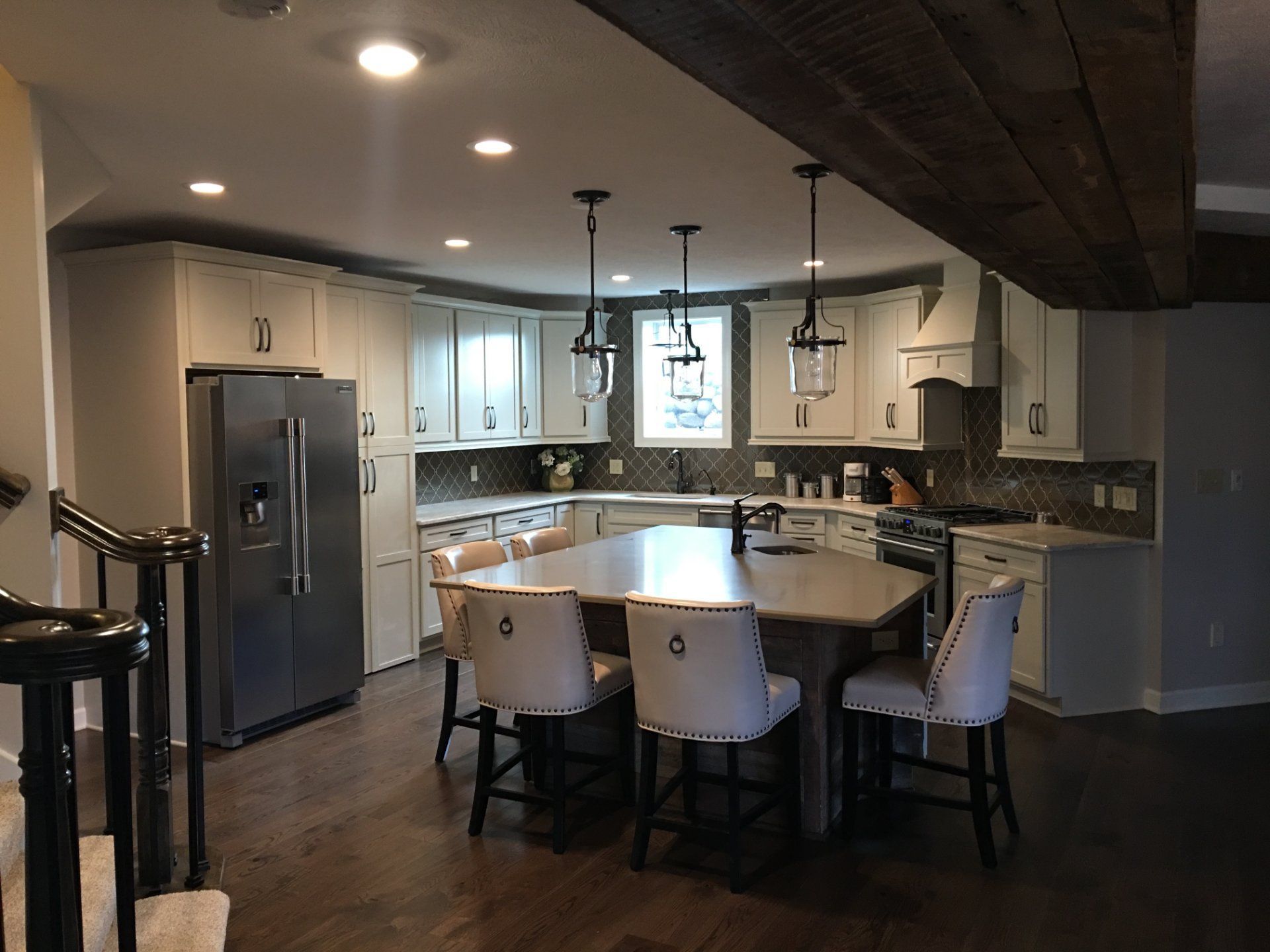 Kitchen with white cabinets, large island with seating, stainless steel appliances, and dark wood beams on the ceiling.