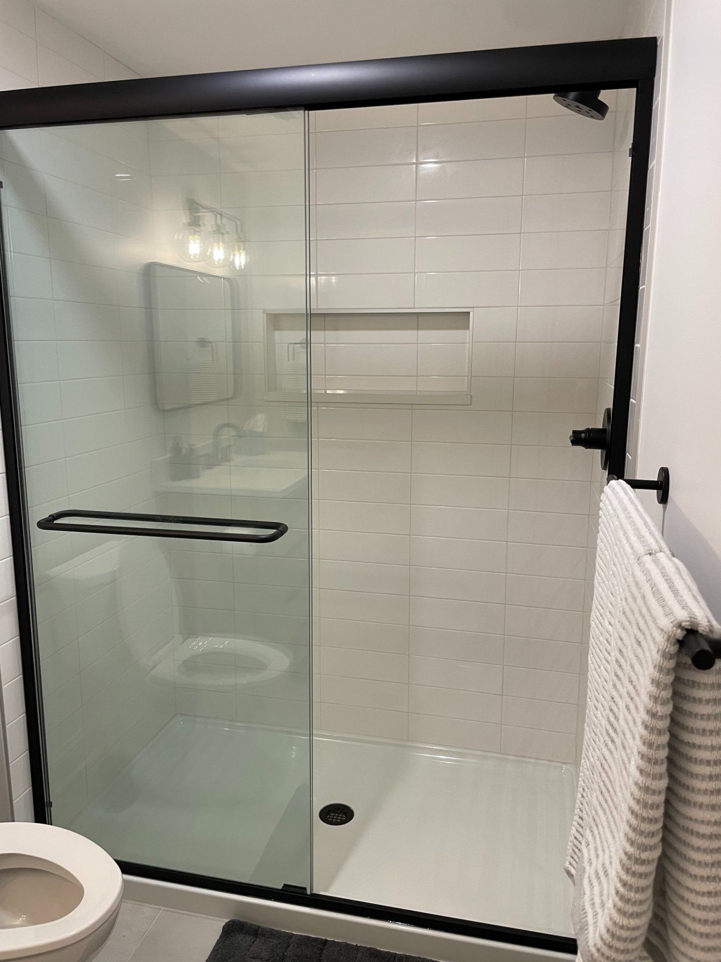 Modern bathroom with white tiled shower, glass door, and black fixtures.