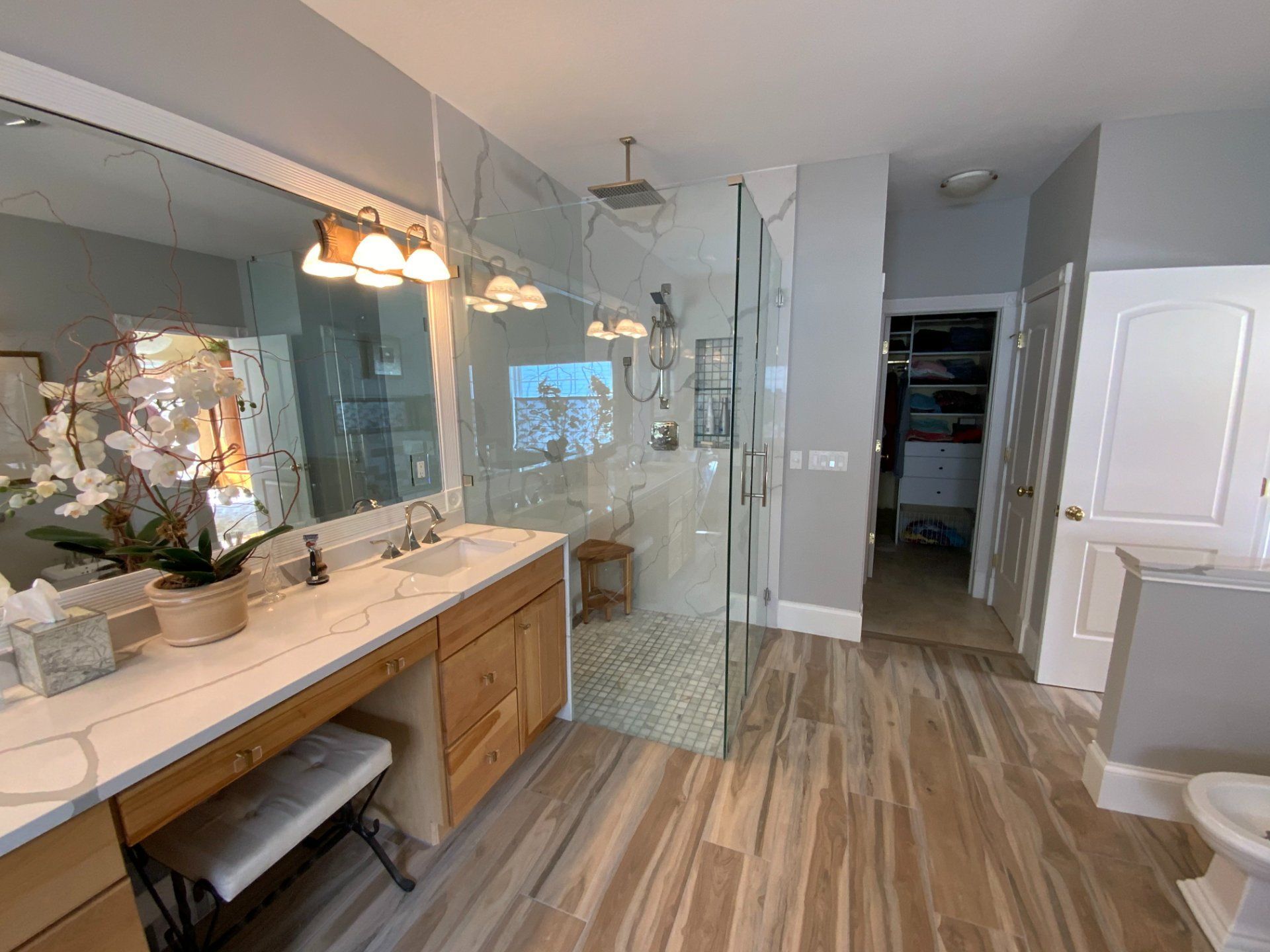Bathroom with wood-look tile floor, large vanity with double sinks, glass shower, and open closet.