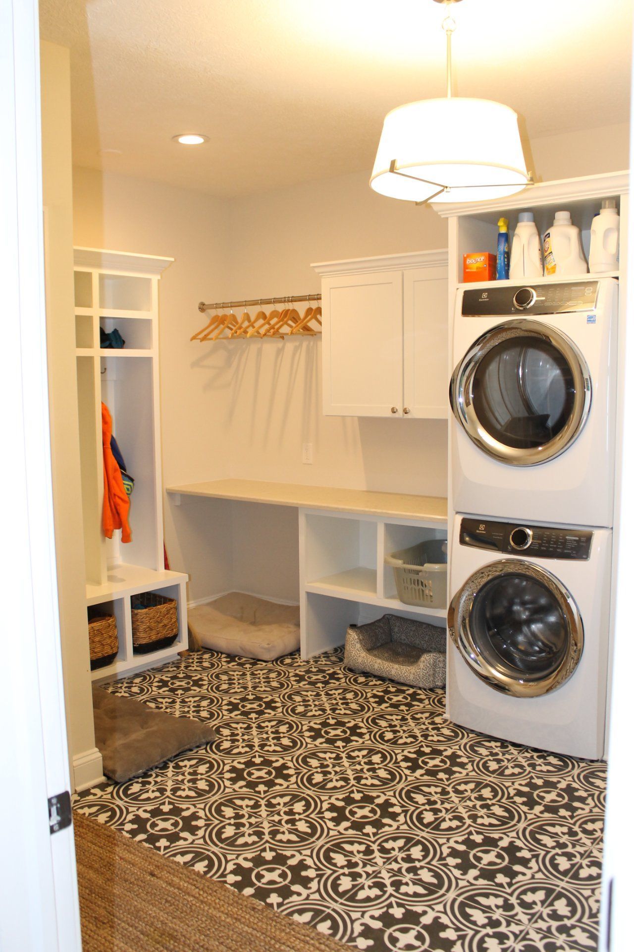 Laundry room with patterned floor, stacked washer/dryer, hanging rack, open shelving, and dog beds.