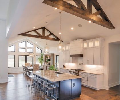 Spacious modern kitchen with vaulted ceiling, wooden beams, island with seating, and white cabinets.