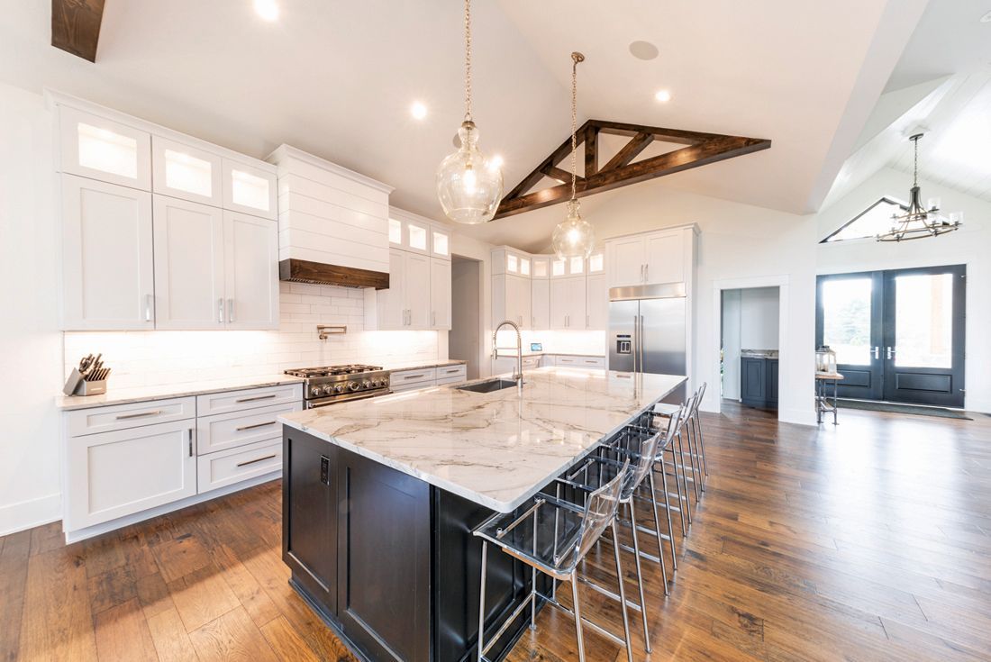 Modern kitchen with white cabinets, dark island, marble countertop, and wood floors.