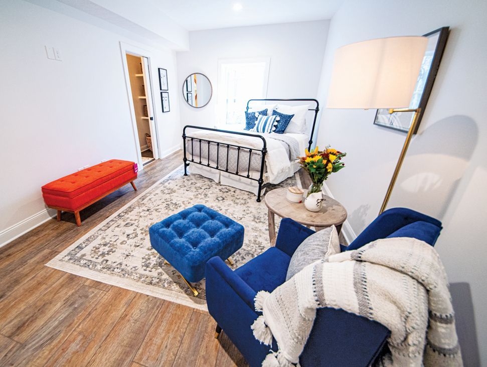 Bedroom with blue armchair, bed, orange bench, rug, and wooden floor.
