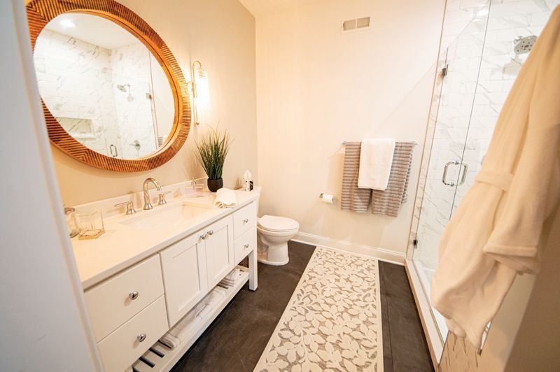 Bathroom with white vanity, large mirror, shower, and patterned floor runner.