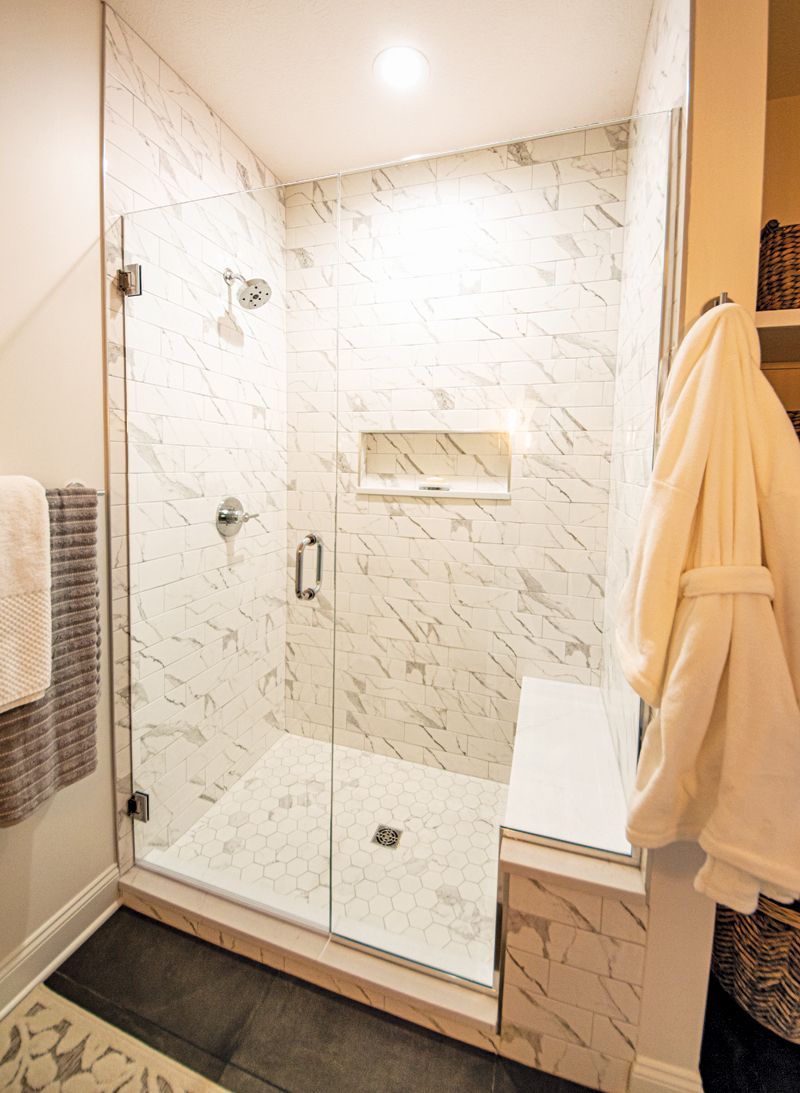 Modern bathroom with marble tile shower and glass door. White robe hangs on the right.