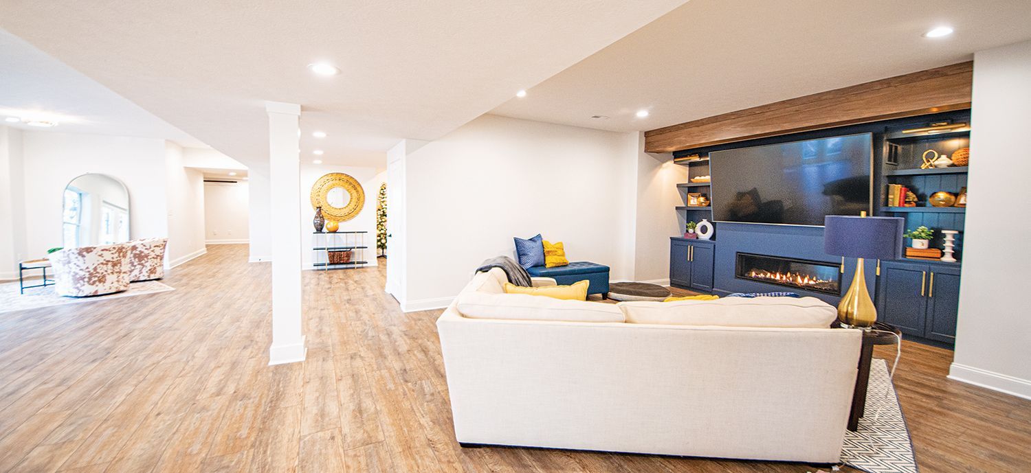 Spacious living room with white walls and wood floors, featuring a fireplace and large TV.