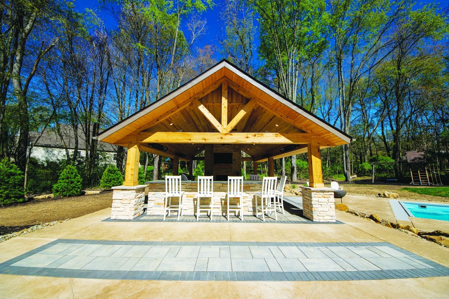 Outdoor pavilion with wooden beams, stone pillars, bar, chairs, and patio.