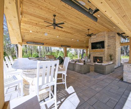 Covered outdoor patio with bar, fireplace, seating, and ceiling fans.