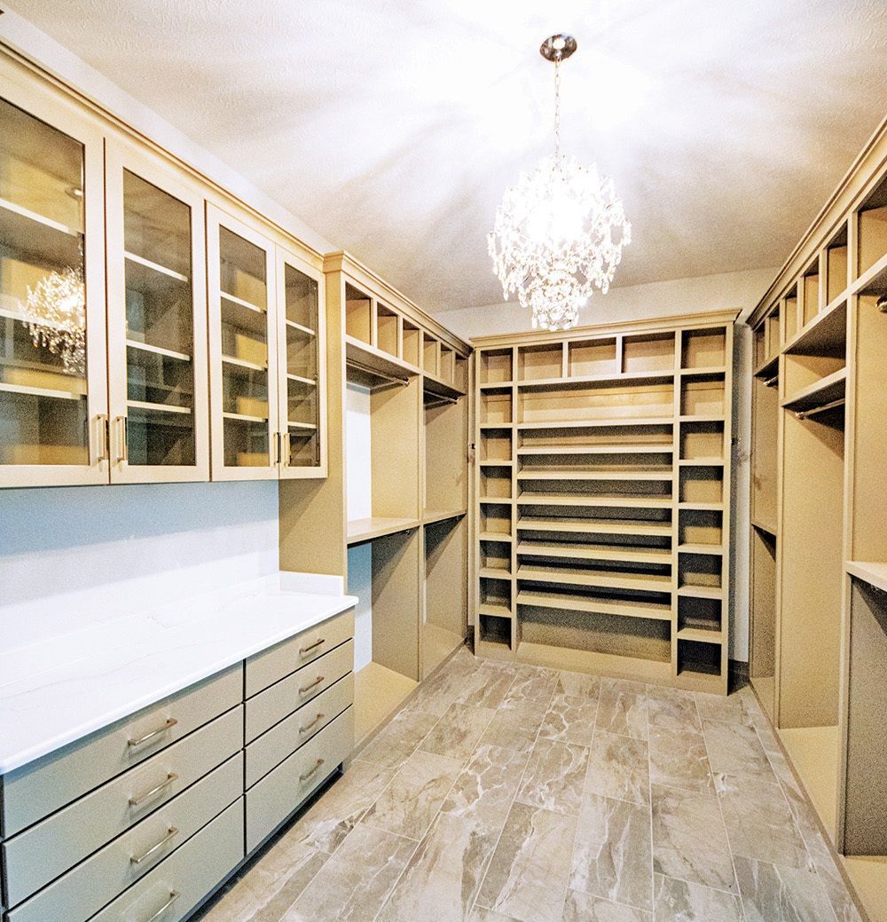 Walk-in closet with built-in shelves, drawers, and glass-door cabinets; neutral colors and a crystal chandelier.