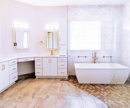 Spacious, bright bathroom with white cabinets, marble tiles, large tub, and a vanity.
