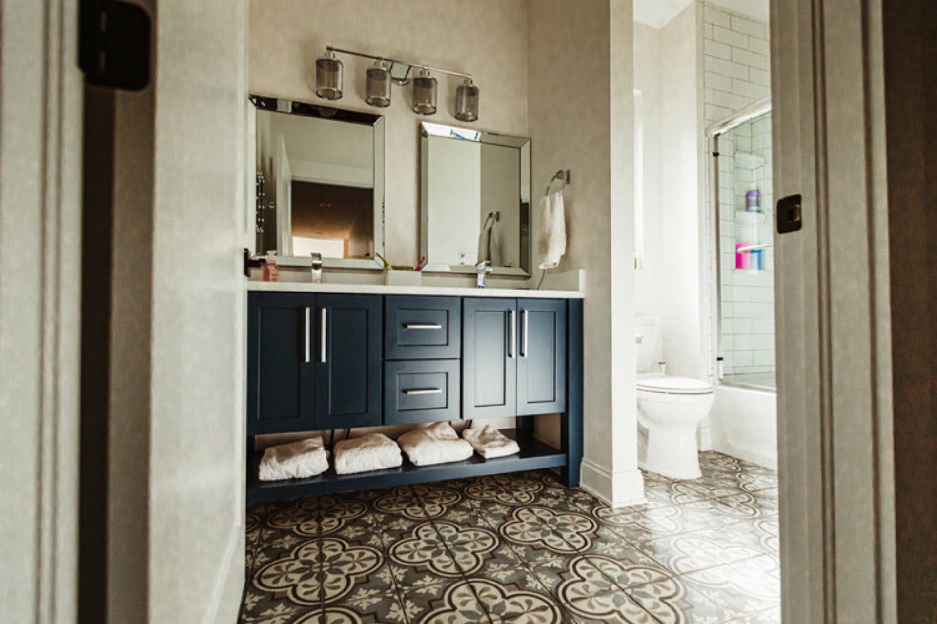 Bathroom with navy vanity, dual mirrors, and patterned tile floor.