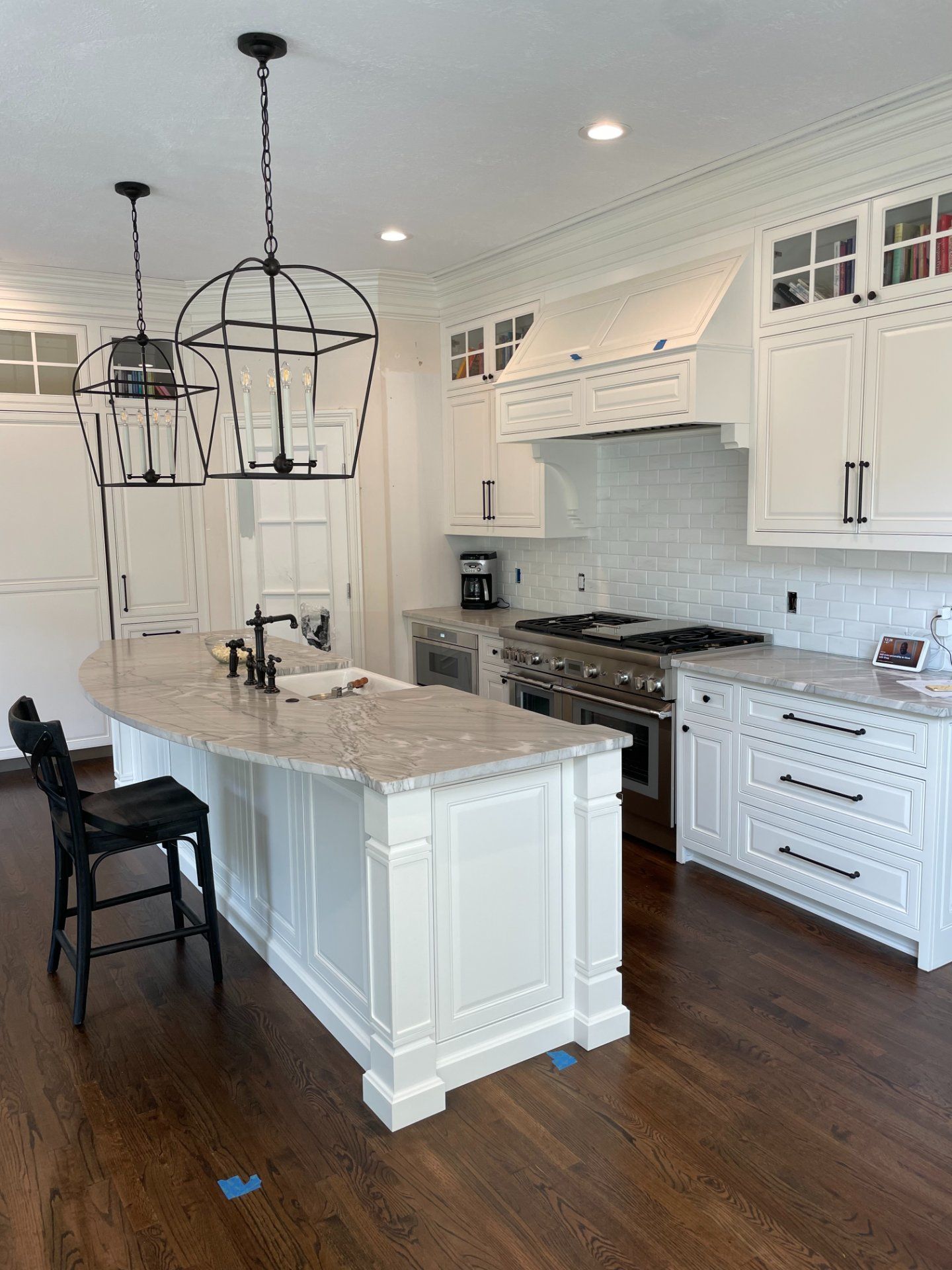 Elegant white kitchen with island, range, and two pendant lights over island with hardwood floors.