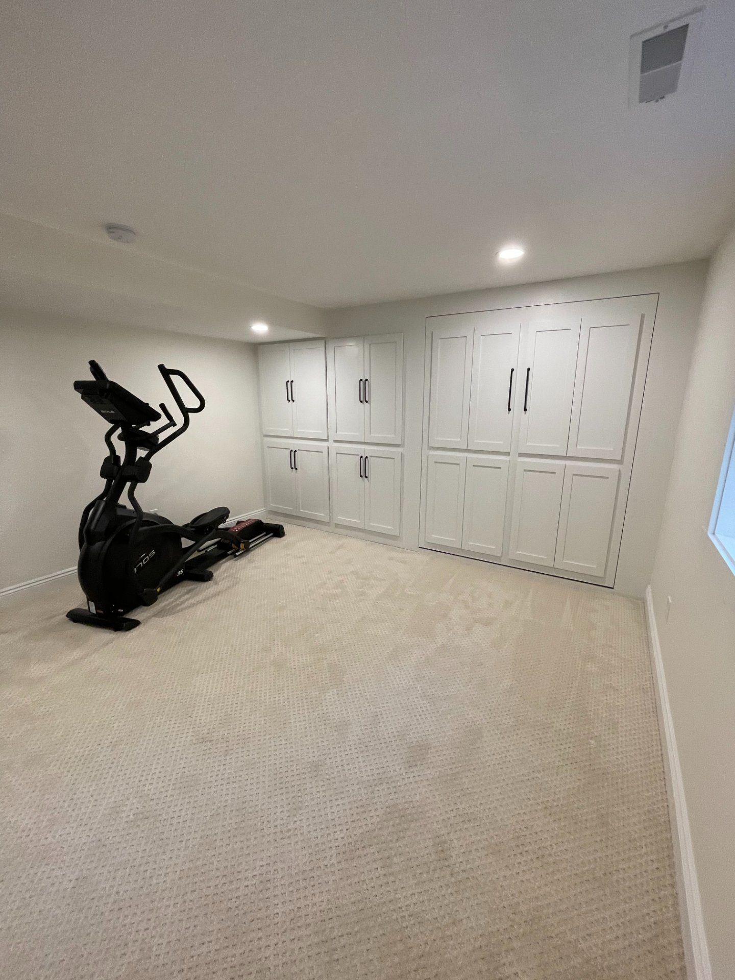 Elliptical machine in a room with white cabinets and beige carpet.