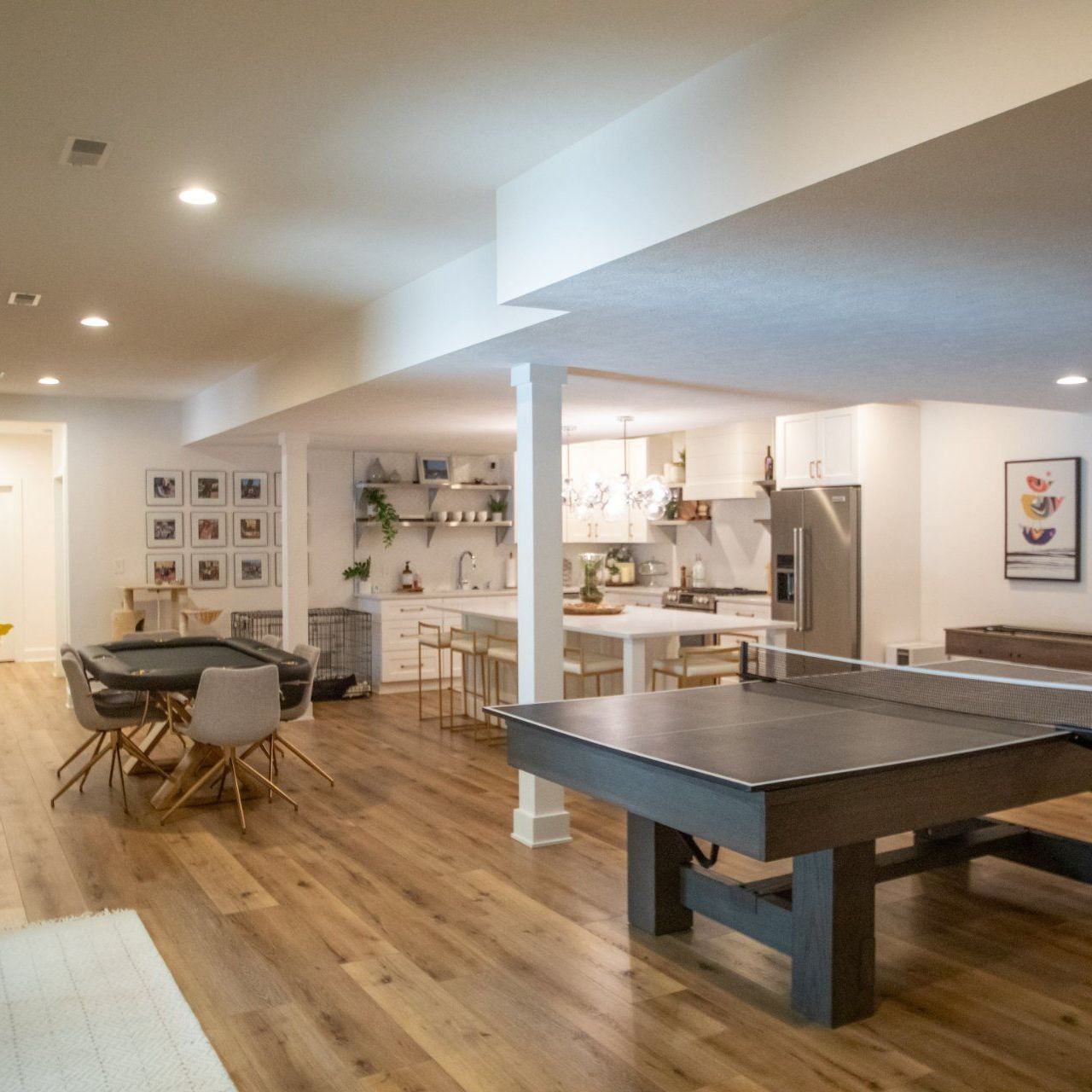 Spacious, modern basement with a kitchen, dining area, and game tables on hardwood floors.