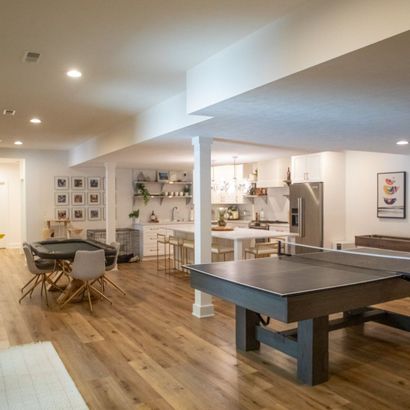Spacious finished basement with game tables, kitchen area, and hardwood floors. White walls and recessed lighting.