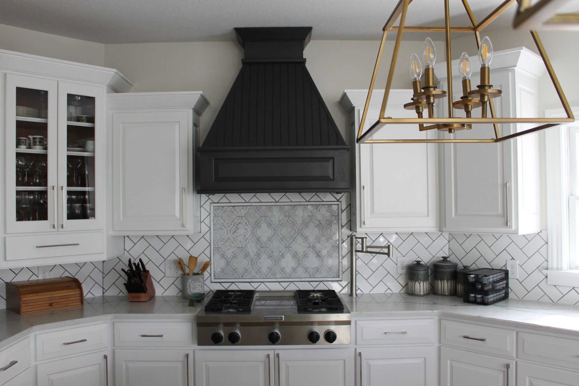 White kitchen with black range hood, stovetop, white cabinets, and geometric backsplash.