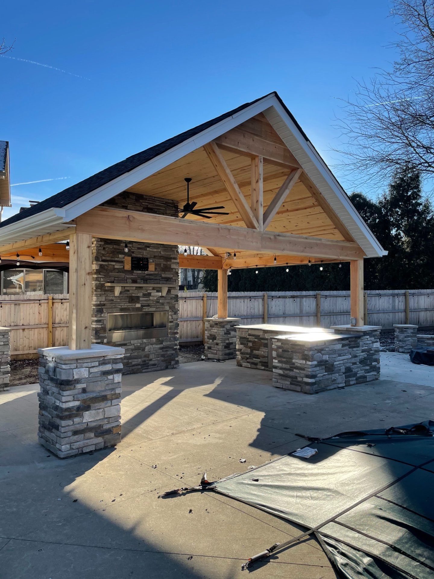 Outdoor pavilion with stone accents and a wooden truss roof on a sunny day.