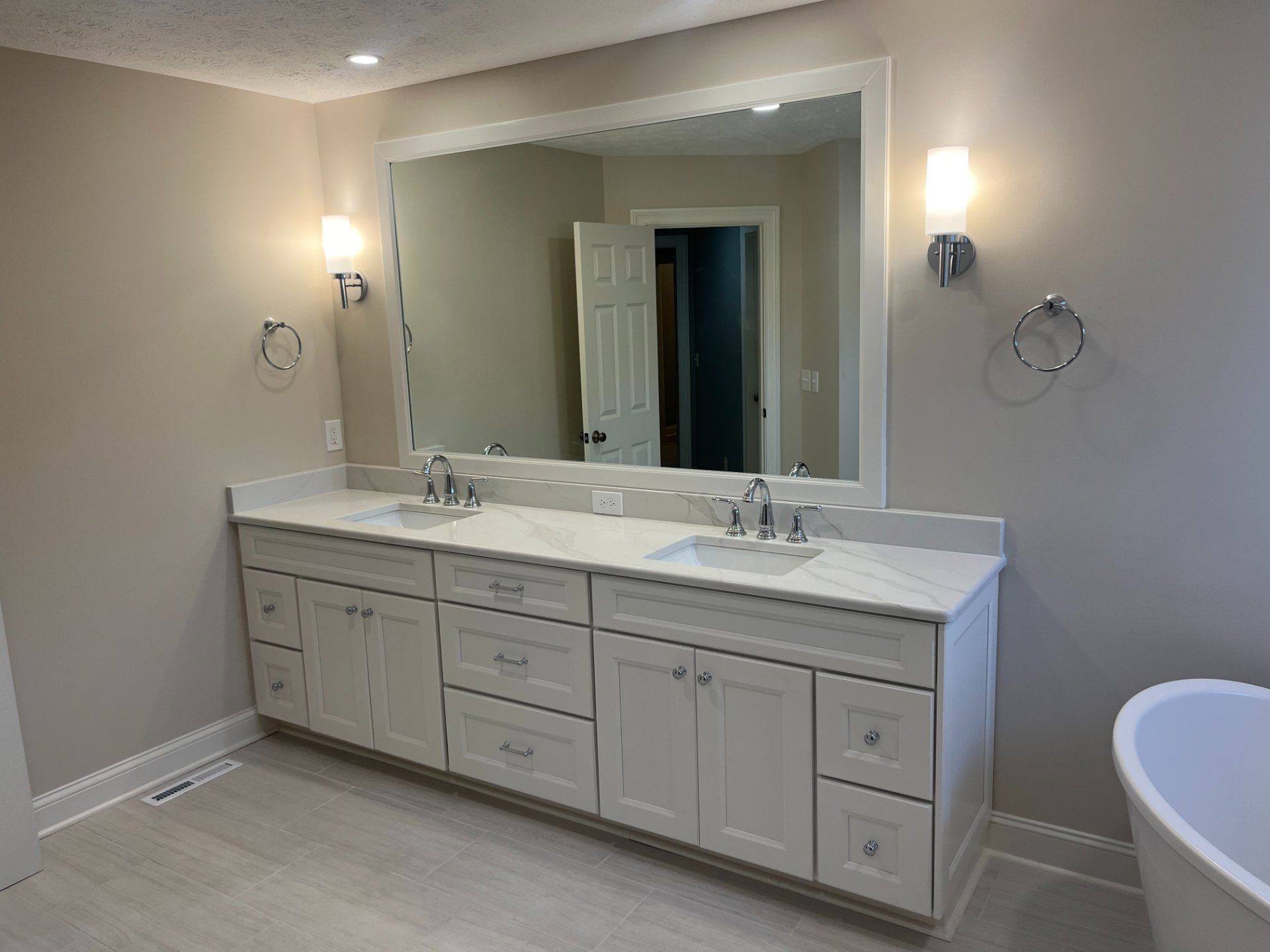 Bathroom with a large mirror above a double vanity. Light-colored cabinetry, countertops, and walls. Silver fixtures.