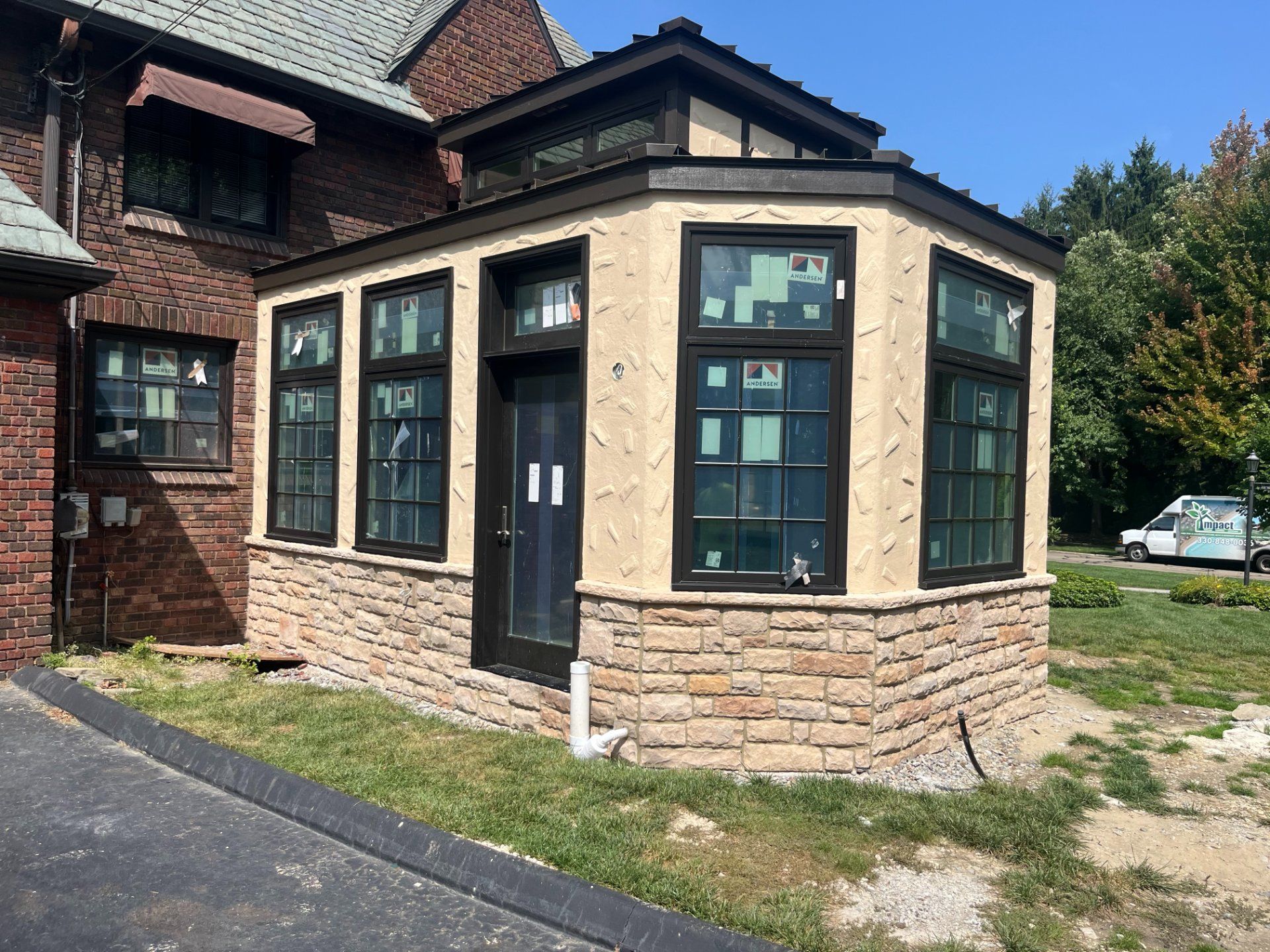 Newly constructed sunroom with stone base and dark-framed windows, attached to a brick building.