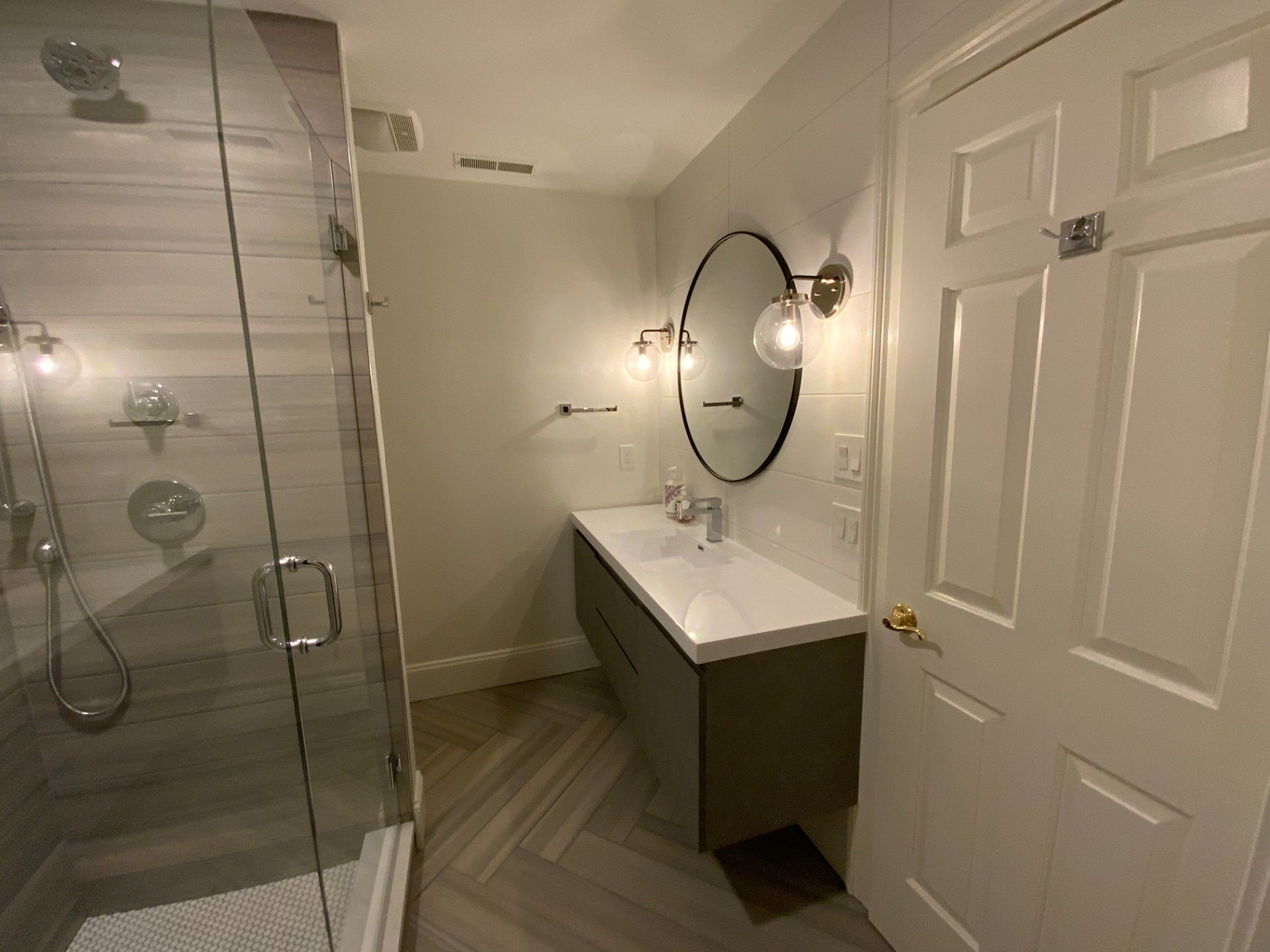 Modern bathroom with a glass shower, vanity, and closed white door.