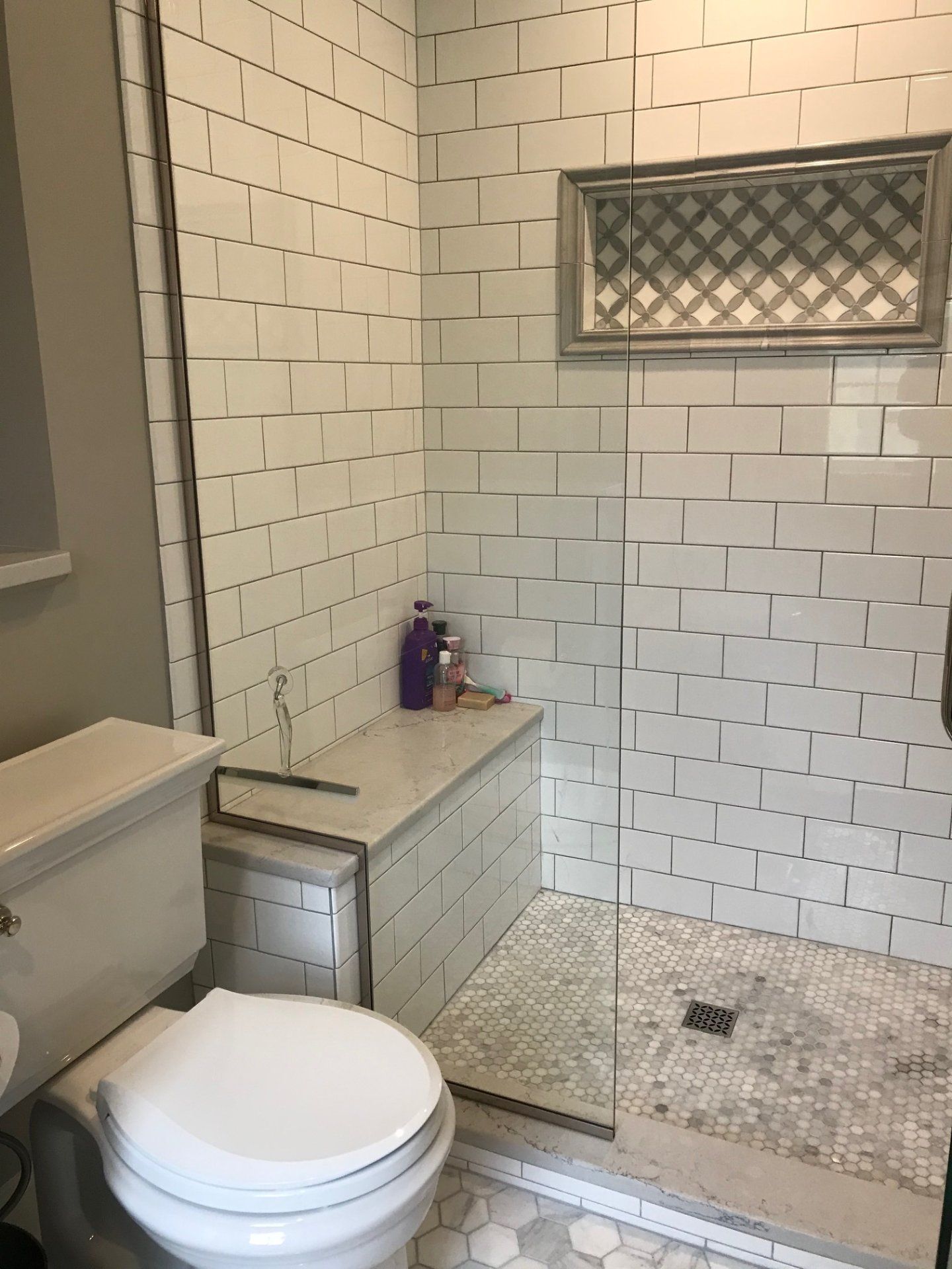 Bathroom with white tile walls, glass shower door, and toilet.