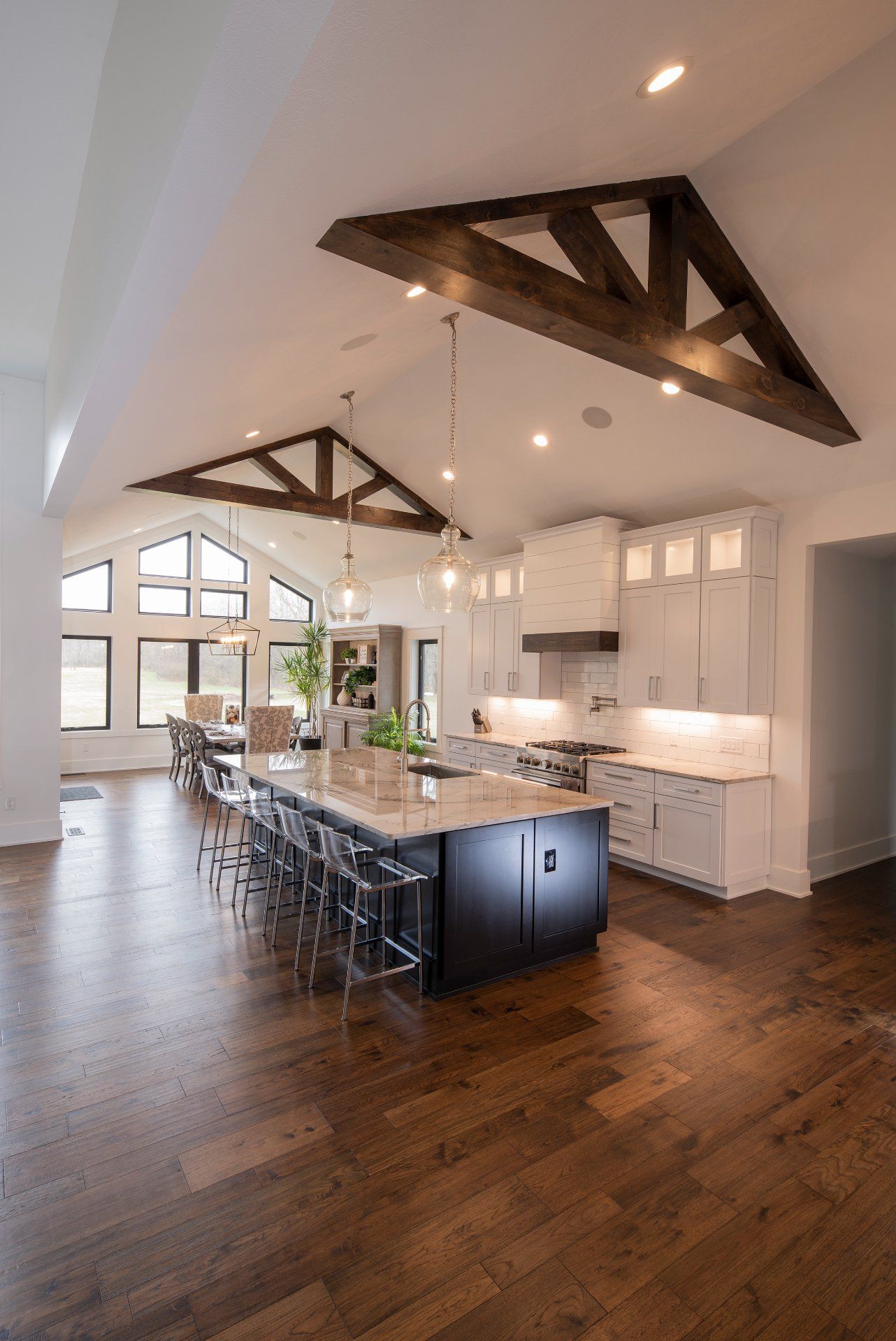 Spacious kitchen with dark wood floor, large island, white cabinets, and exposed wooden beams.