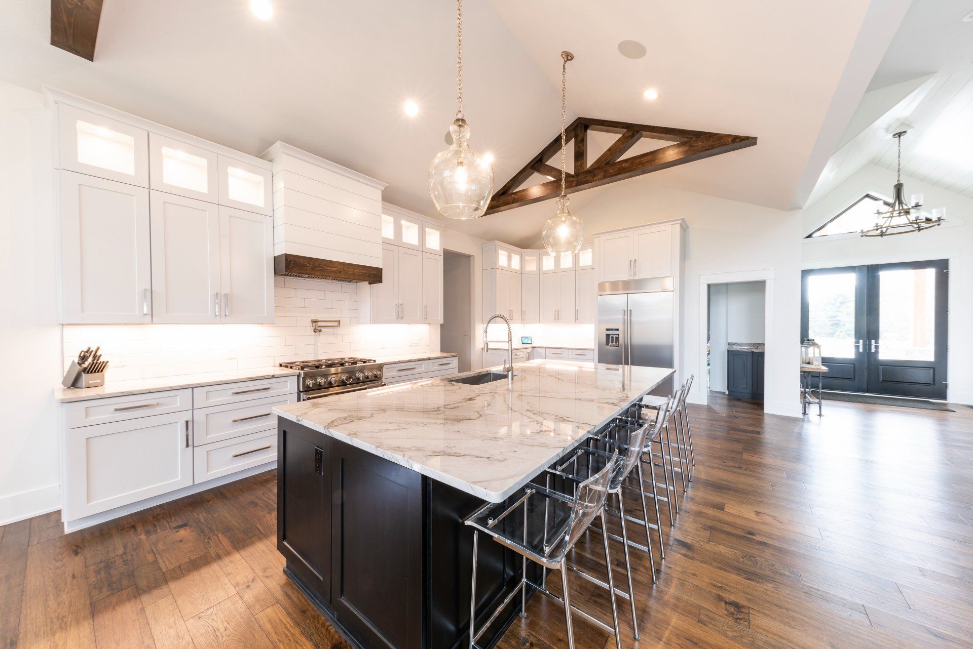 Spacious modern kitchen with white cabinetry, black island, marble countertop, hardwood floors, and overhead lighting.