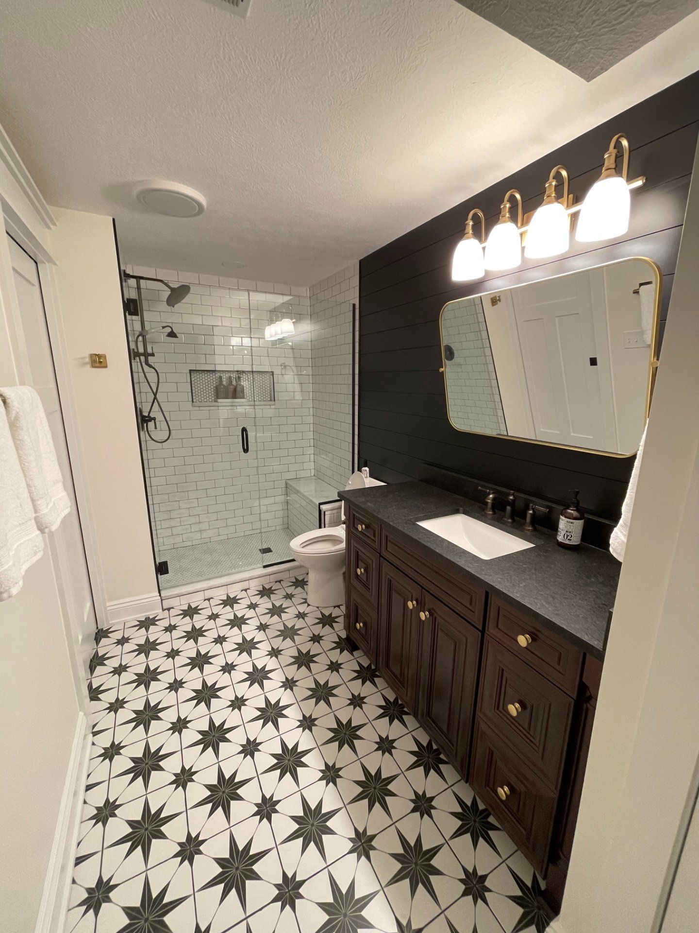 Bathroom with star-patterned floor, dark vanity, and glass shower. Black and white tiles, gold accents.