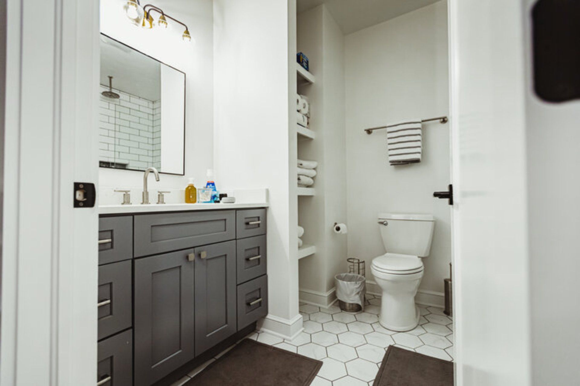 Bathroom with gray vanity, toilet, and open shelving; white walls, patterned floor.