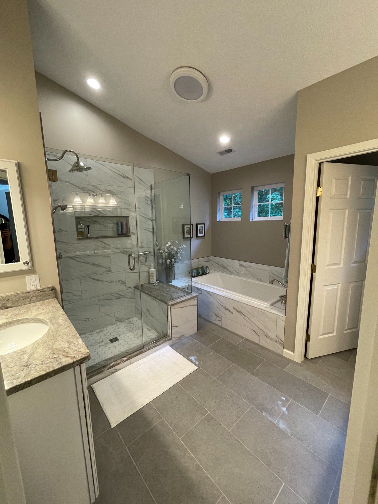 Spacious bathroom with glass shower, marble tile, bathtub, and two windows.