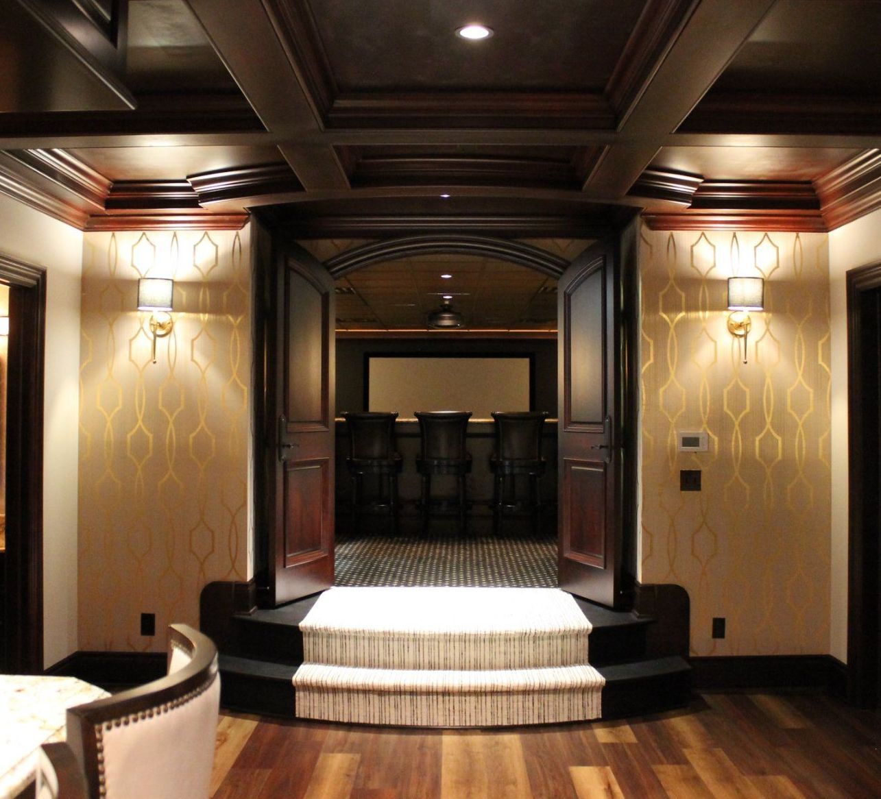 Theater room entrance with steps, dark wood trim, sconces, and a projector screen visible in the background.
