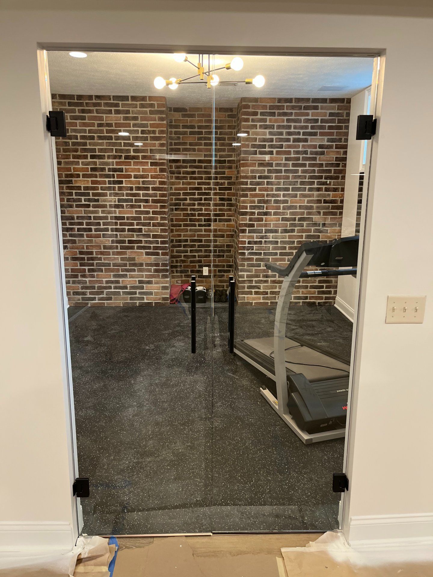 Glass door leading to a home gym with a treadmill and brick wall.
