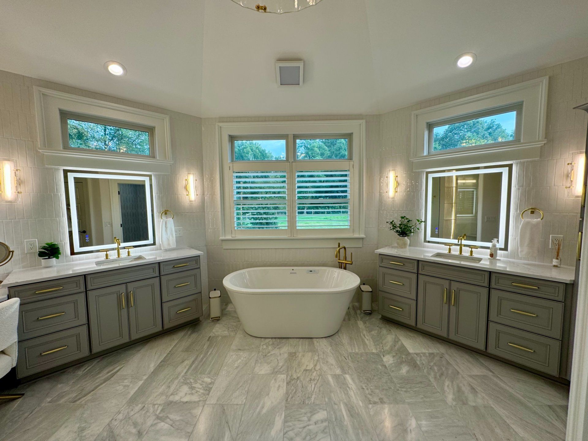 Luxurious bathroom with gray vanities, white tub, marble floor, and large windows.