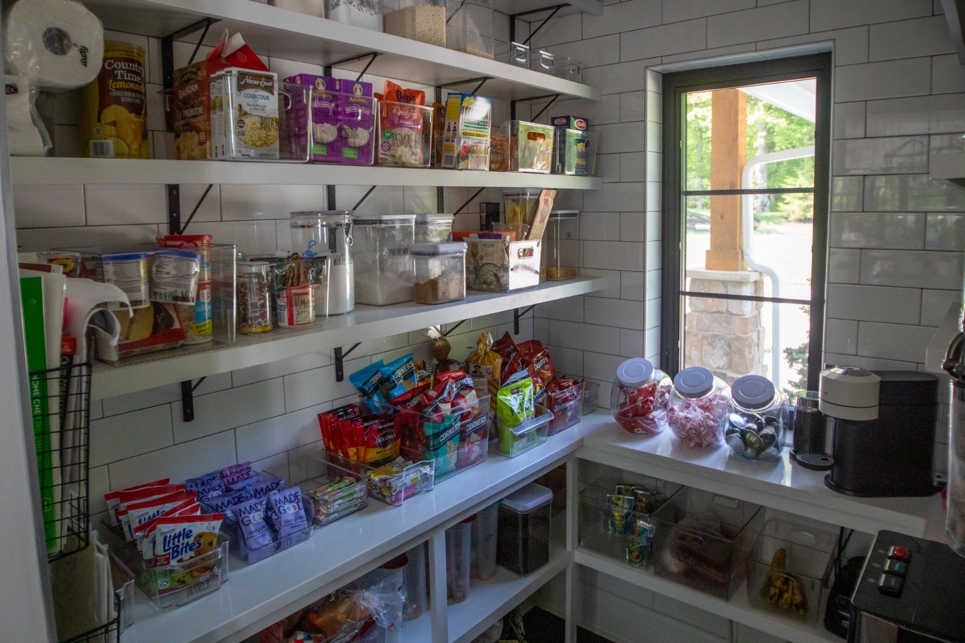 Pantry with white shelves filled with packaged and jarred food items. Window visible on the right.