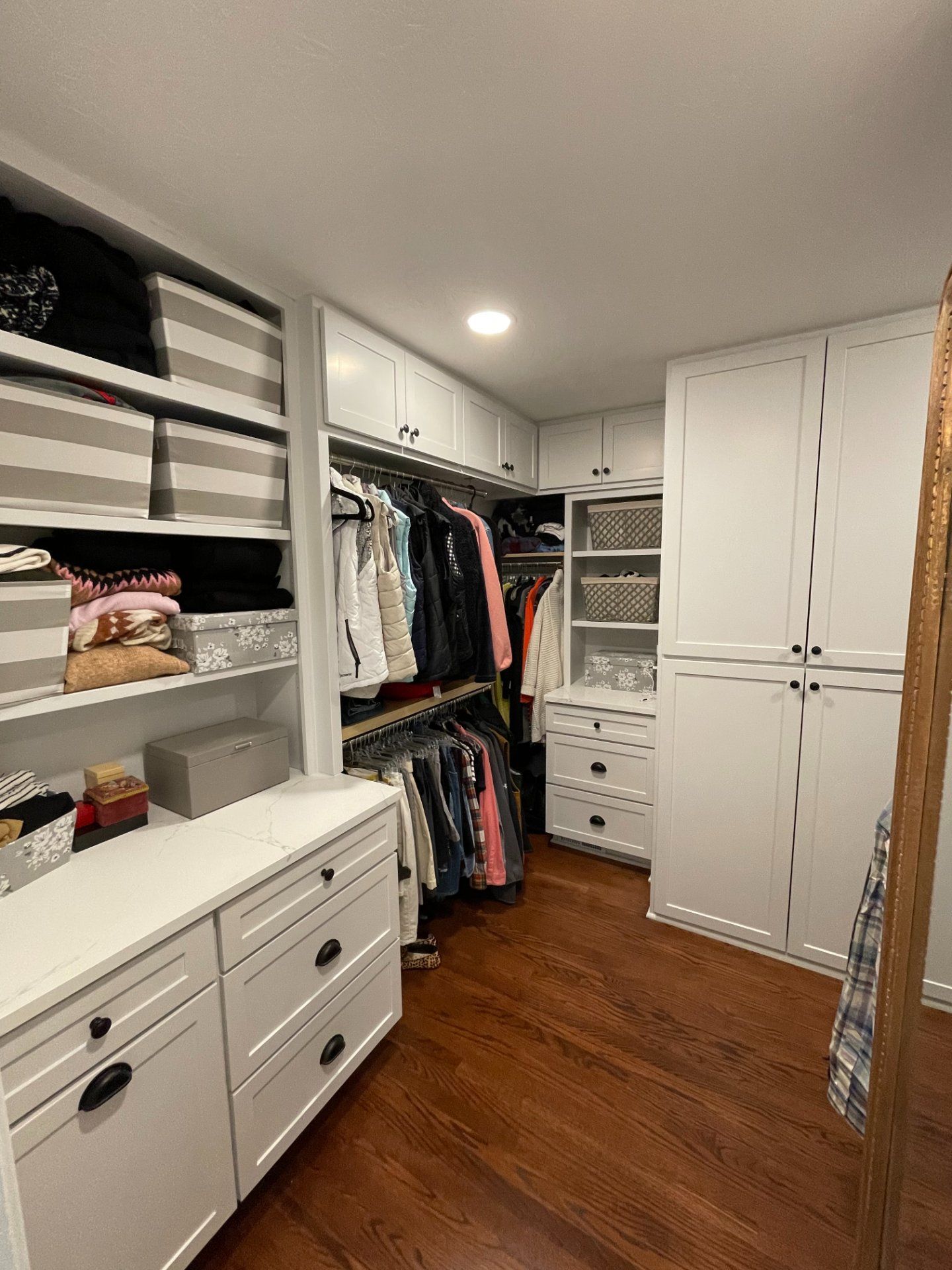 Walk-in closet with white cabinets, dark wood floor, and hanging clothes.