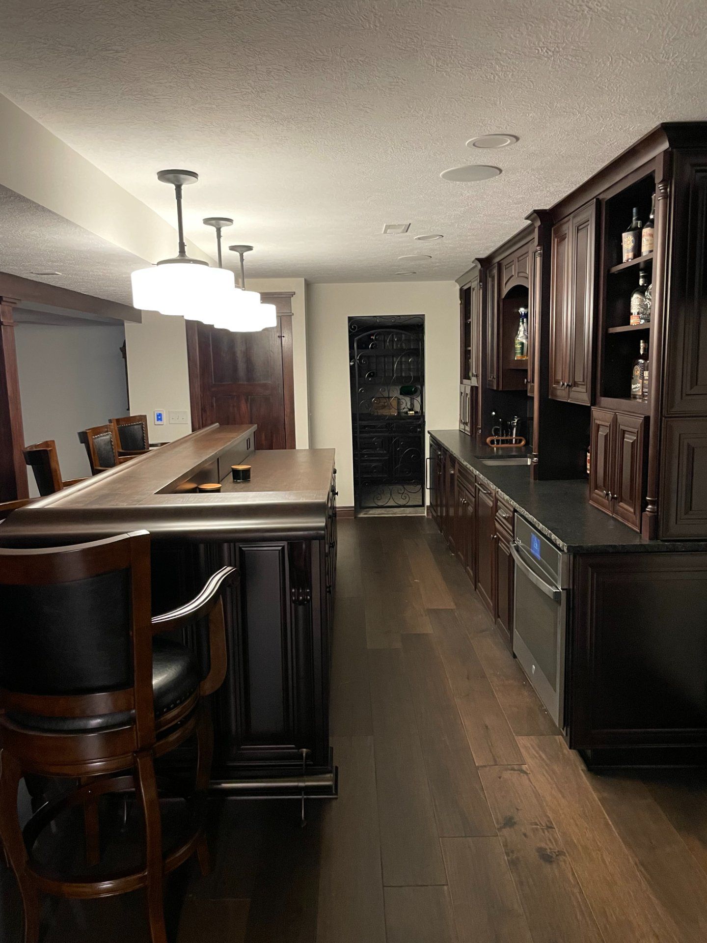 Dark wood bar with seating, cabinetry, and a walk-in wine cellar in a basement.