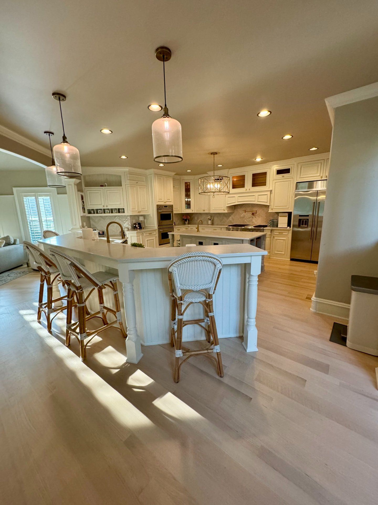 Bright, open kitchen with white cabinets, island, wooden floors, and pendant lights.