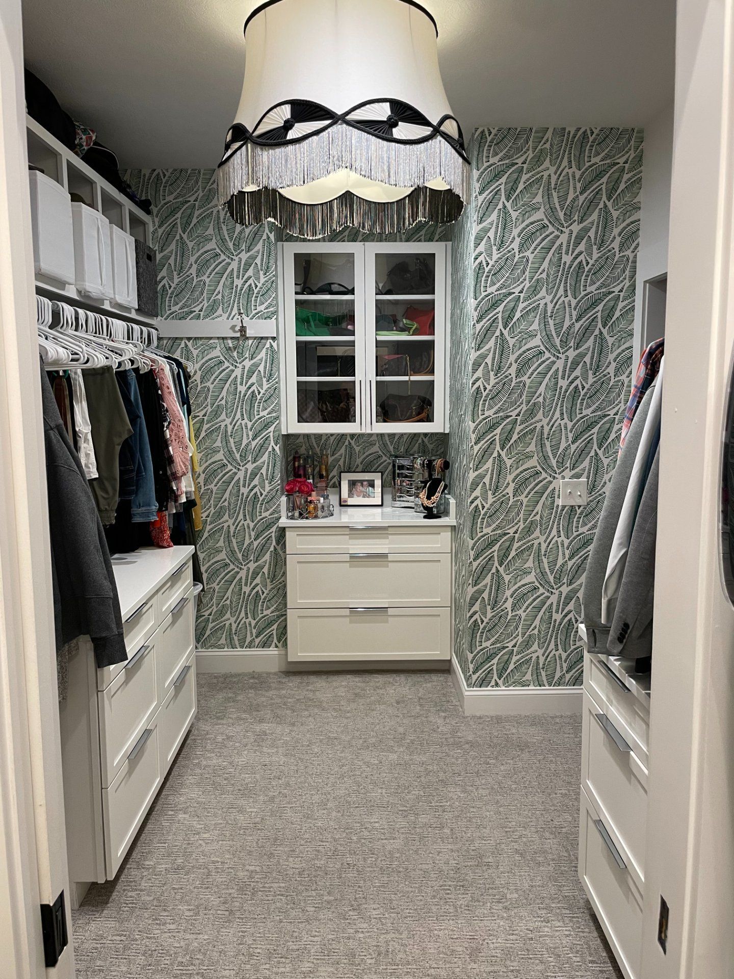 Walk-in closet with white cabinets, green patterned wallpaper, and a decorative lampshade.