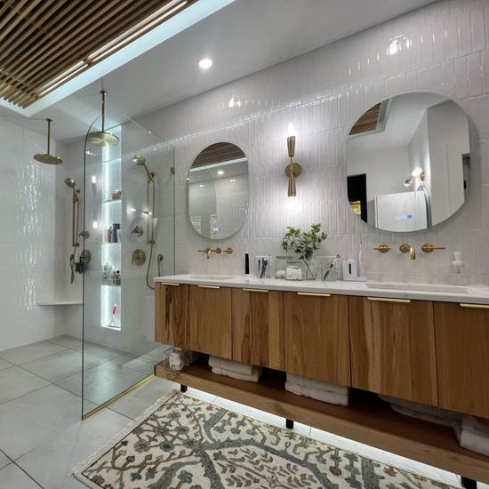Modern bathroom with wooden vanity, two round mirrors, and glass shower.