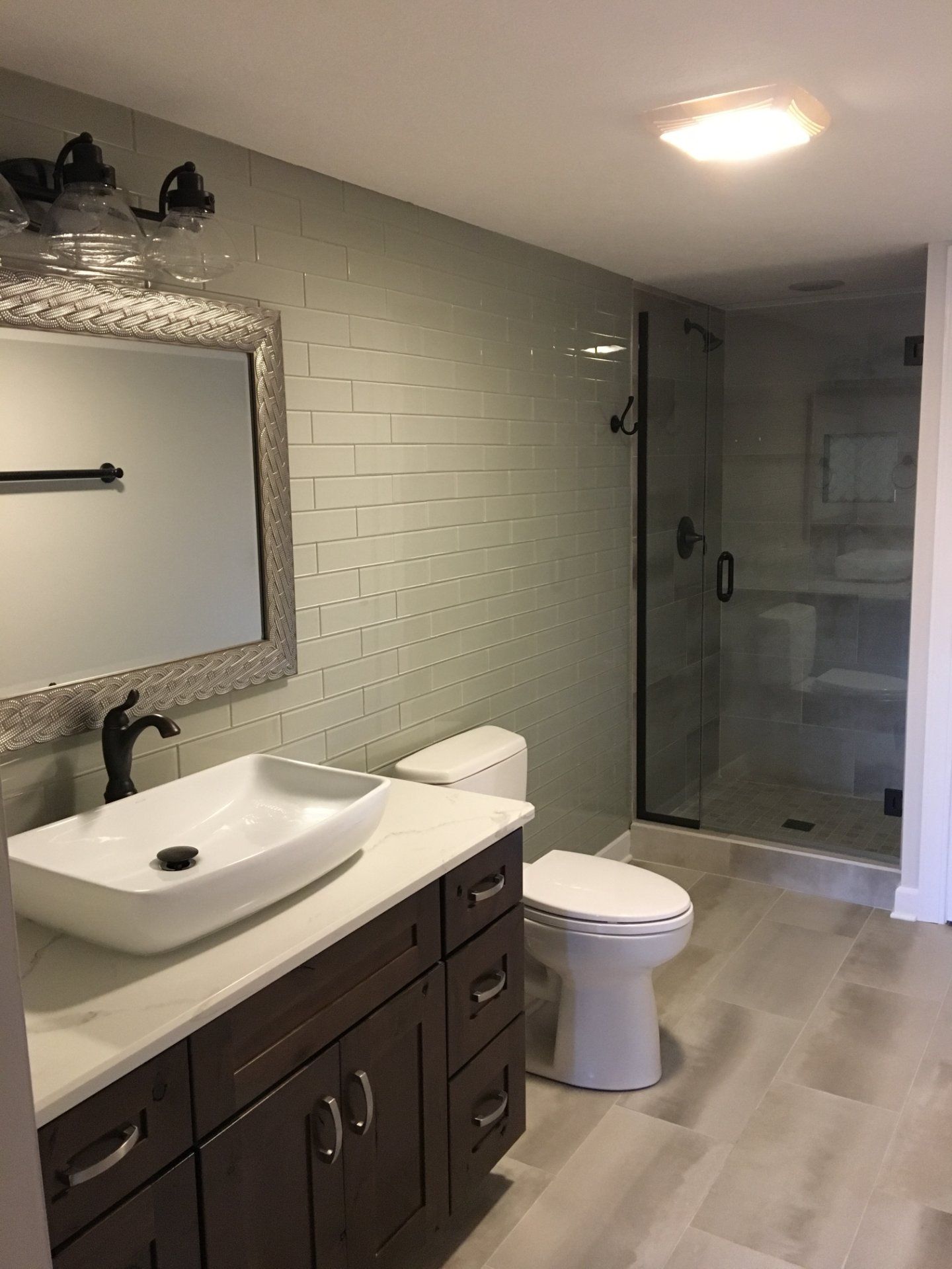 Modern bathroom with dark brown vanity, vessel sink, tiled walls, and a glass shower.
