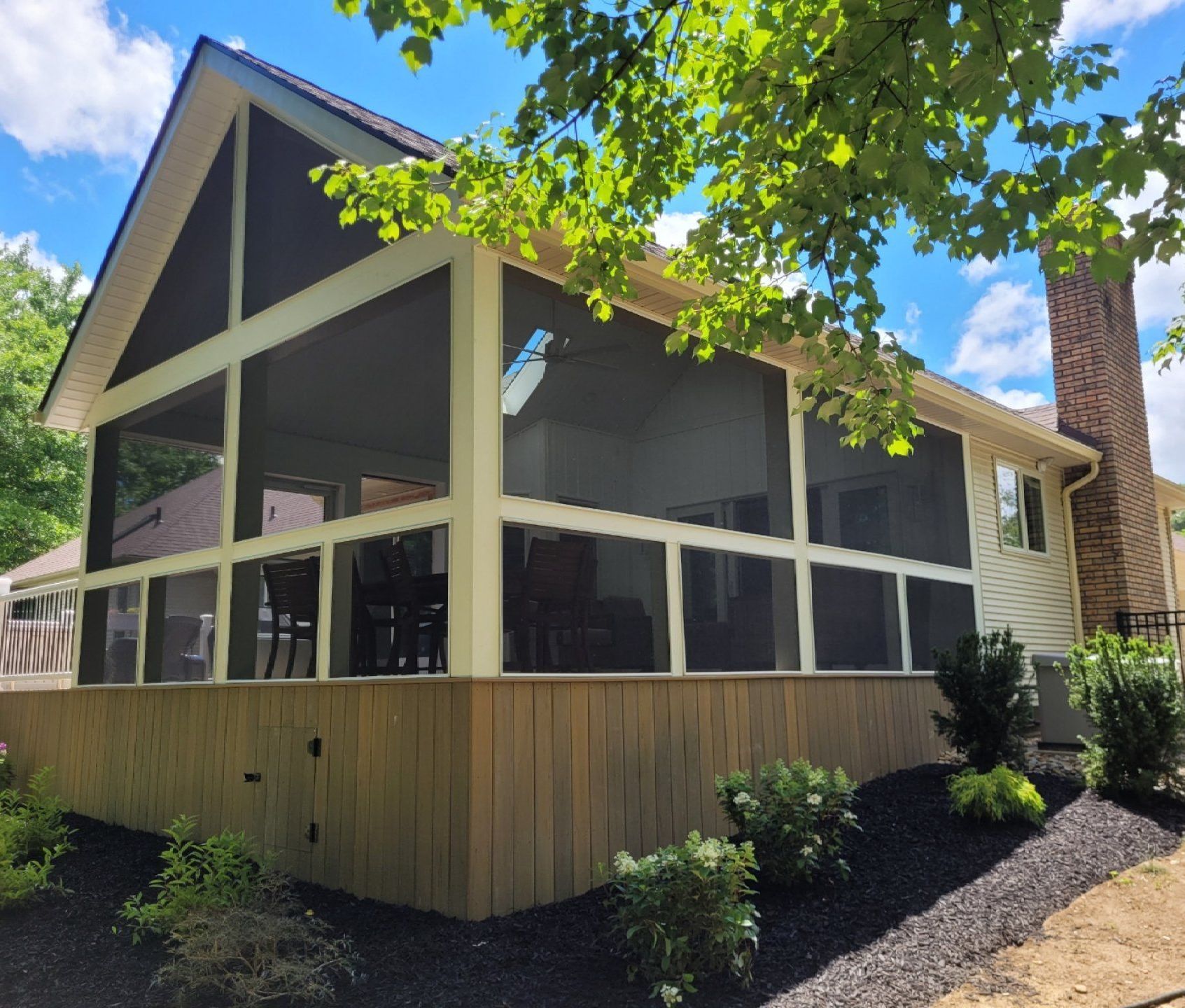 Screened-in porch addition with wood siding and a gabled roof. A brick chimney and landscaping are visible.